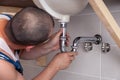 Closeup male plumber worker in blue denim uniform, overalls, fixing sink in bathroom with tile wall. Professional Royalty Free Stock Photo