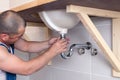 Closeup male plumber worker in blue denim uniform, overalls, fixing sink in bathroom with tile wall. Professional Royalty Free Stock Photo