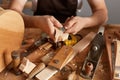 Closeup of man carpenter wearing white t-shirt, black cap and brown apron working, uses chisel for cutting shapes and curves in Royalty Free Stock Photo