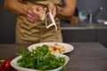 Closeup man cooking dinner at home, preparing Italian pasta with tomato sauce and pouring grated parmesan cheese. A bowl Royalty Free Stock Photo