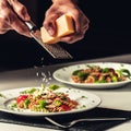 Closeup of the man grating a piece of cheese on a pasta salad on a plate with a black background Royalty Free Stock Photo