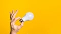 Closeup man hand holding white led light bulb against yellow background. concept of ideal, environment ecology and energy Royalty Free Stock Photo