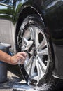 Closeup man hand washing new car alloy silver wheels with bristle scrub brush, soap suds and bucket Royalty Free Stock Photo