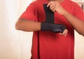 Closeup man in red shirt wearing black wrist brace support on right hand, tightening velcro using other arm Royalty Free Stock Photo