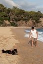 Closeup of a man  walking his dog along a sandy beach, with the waves of the ocean in the background Royalty Free Stock Photo