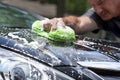 Closeup man washing new black car hood with big soft sponge, soap suds and bucket Royalty Free Stock Photo