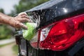 Closeup man washing new black car rear tail light with big soft sponge, soap suds Royalty Free Stock Photo