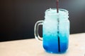 mason jar glass of cold fresh blue lagoon cocktail with ice on table and blurred dark background