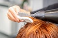 Closeup of master's hand with blow-drying and hairbrush blowing female red hair in a salon. Royalty Free Stock Photo