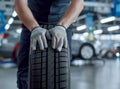 Closeup of mechanic hands pushing a black tire in the workshop. Royalty Free Stock Photo