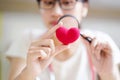 Closeup medical student holding a magnifying glass and looks at a yarn red heart on blurred background. Royalty Free Stock Photo