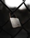 Closeup of a metal padlock hanging from a chain link fence, secured with a clasp