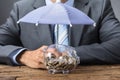 Businessman Sheltering Transparent Piggybank With Umbrella