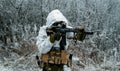Closeup military man in white camouflage uniform with hood and aims of the machinegun. Horizontal photo side view