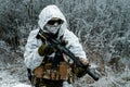 Closeup military man in white camouflage uniform with hood and machinegun. Horizontal photo side view