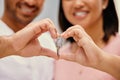 Closeup of a mixed race couple smiling making a heart gesture with their hands holding a key in their new house together Royalty Free Stock Photo