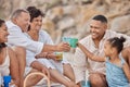 Closeup of a mixed race family having a picnic on the beach and smiling while having some food with snacks. Happy family Royalty Free Stock Photo