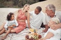 Closeup of a mixed race family having a picnic on the beach and smiling while having some food with snacks. Happy family Royalty Free Stock Photo