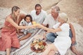 Closeup of a mixed race family having a picnic on the beach and smiling while having some food with snacks. Happy family Royalty Free Stock Photo