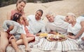Closeup of a mixed race family having a picnic on the beach and smiling while having some food with snacks. Happy family Royalty Free Stock Photo