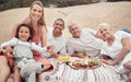 Closeup of a mixed race family having a picnic on the beach and smiling while having some food with snacks. Happy family Royalty Free Stock Photo