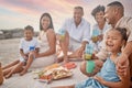 Closeup of a mixed race family having a picnic on the beach and smiling while having some food with snacks. Happy family Royalty Free Stock Photo