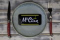 Closeup of mobile phone on plate and wood table, cutlery with logo lettering of mccain food company