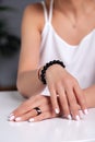 Closeup model hands with manicure, white nails, black ring with stone, bracelet made of shiny black beads, red, beige braided