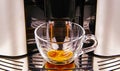 Closeup of modern fully automatic coffee maker machine outlet, one isolated transparent glass cup filling with fresh brewed cafe