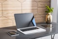 Closeup of modern laptop with smartphone, digital tablet and bronze color vase on dark glossy table in sunny modern interior