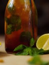 Closeup of a moist bottle of cool tea with leaves of mint, and halves of lime. A glass bottle with a refreshing cool