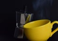 Closeup of a Moka pot and yellow mug isolated in the black background