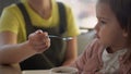 Closeup mom feed young baby in white feeding up high chair, kid is trying to eat himself, happy child with food stained Royalty Free Stock Photo