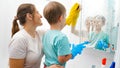 Closeup of mother and little son cleaning and washin mirror in bathroom with sponges and chemical detergent Royalty Free Stock Photo