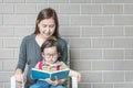 Closeup asian mother is teaching her son to read a book on stone brick wall textured background with copy space Royalty Free Stock Photo