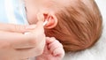 Closeup of mother using cotton swabs to clean little baby's ears from ear wax. Concept of babies and newborn hygiene and Royalty Free Stock Photo