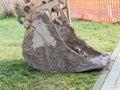 Closeup of muddy excavator shovel on grass near construction are