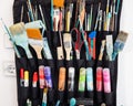 Closeup of colorful dirty paintbrushes, markers and other artistic tools organized in black holder on the white wall Royalty Free Stock Photo