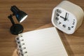 Closeup a note book with light from small lamp and white alarm clock on wood desk in dark room textured background