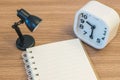 Closeup a note book with small lamp and white alarm clock on wood desk textured background