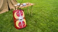 Closeup of an old roman shield leaning on a small wooden tree near a tent in a field