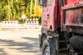 Closeup of old rusty and dirty red truck side, paint peeling on cargo area wall, large tires visible, blurred road block sign and Royalty Free Stock Photo