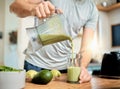 Closeup of one caucasian man pouring healthy green detox smoothie from blender into glass in kitchen at home. Guy having