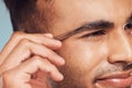 Closeup of one handsome young indian man using a tweezer to remove hair from his eyebrows. Face of a mixed race guy