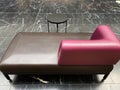 Closeup of one isolated empty purple brown leather chaiselongue with small round table on black and white marble floor