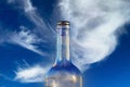 Closeup of one single isolated empty transparent red wine alcohol glass bottle, clear blue sky and fluffy white cloud background Royalty Free Stock Photo