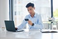 Closeup of one young asian businessman spending money online with a credit card and phone in an office. Making purchase Royalty Free Stock Photo