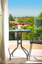 Closeup of open balcony with summer garden landscape view. Terrace patio with glass table, chairs and red drink glasses