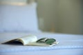 Closeup of open book and sun glasses laying on white bed in blur bedroom background Royalty Free Stock Photo