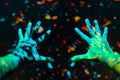 Closeup of open neon painted hands on a dark background with blurred paint splashes